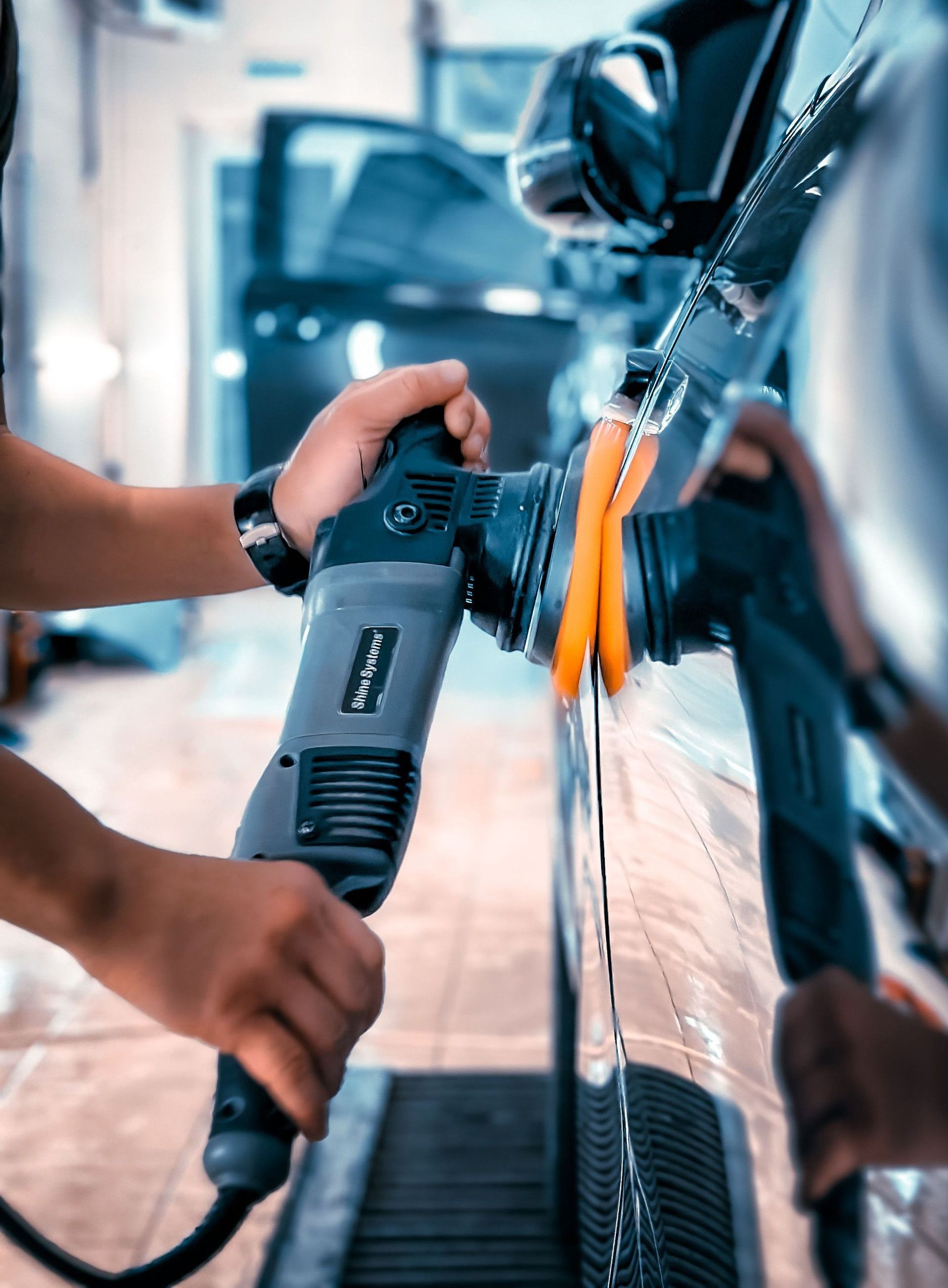 Close-up of a man polishing a car in a garage using an electric buffer tool, showcasing car maintenance.